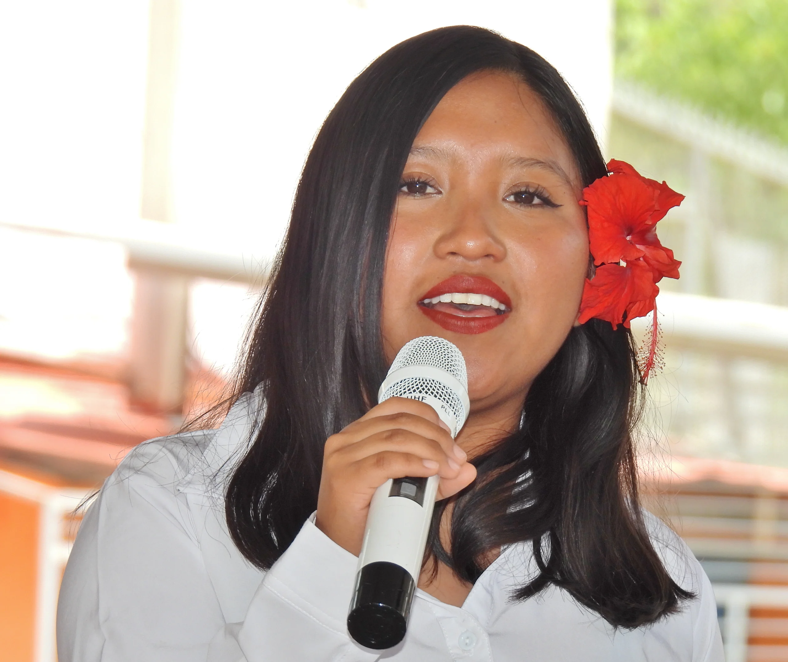 Alumna con una flor roja en el cabello hablando al micrófono