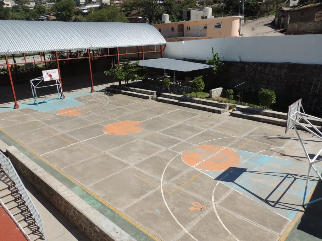 Cancha al aire libre con piso de colores, tableros y un muro de piedra, vista desde arriba