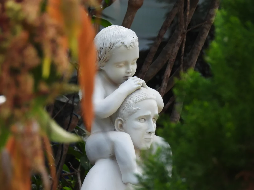 Escultura blanca de dos niños entre plantas