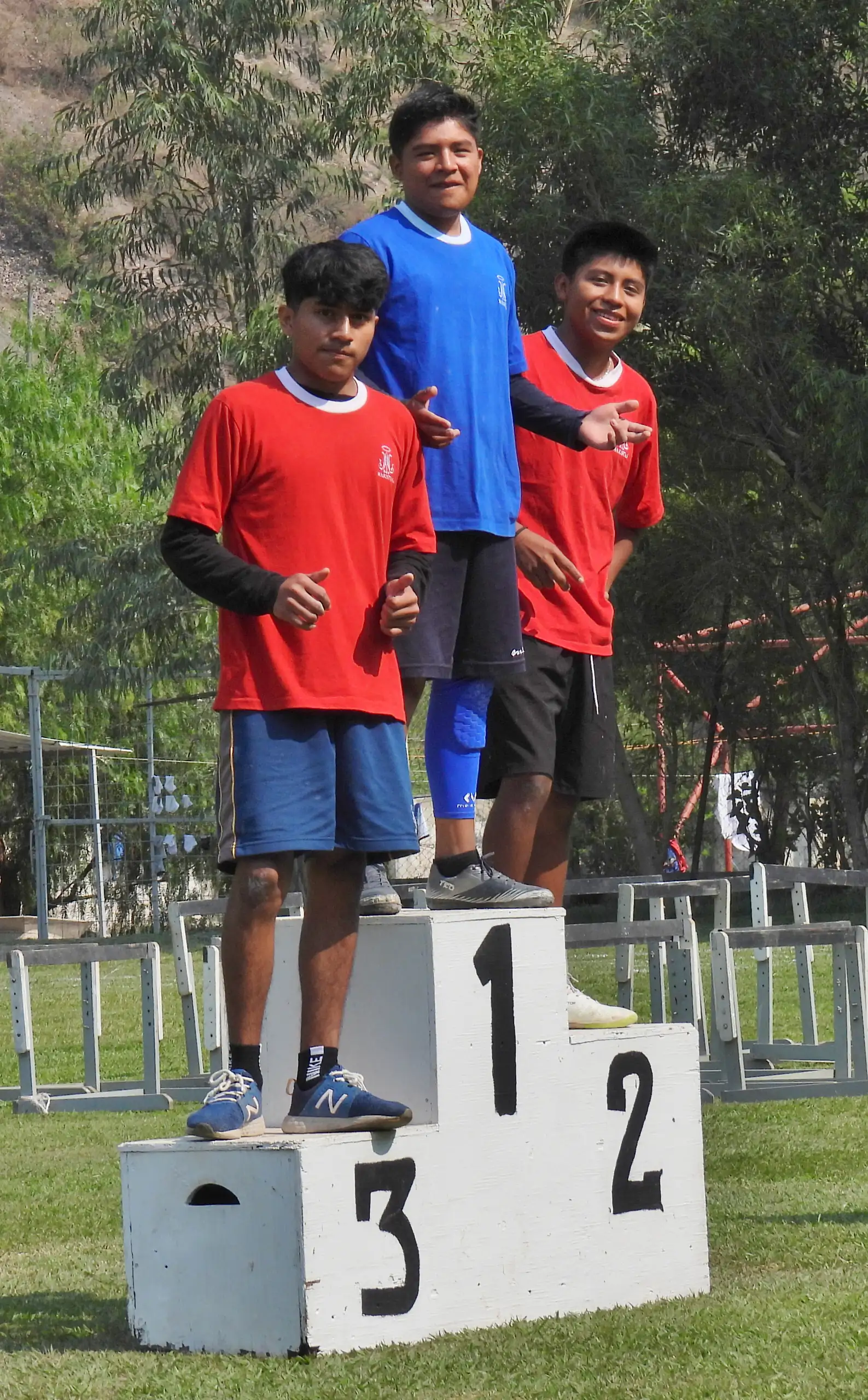 Alumnos de playera roja y azul sobre el podio de primero, segundo y tercer lugar