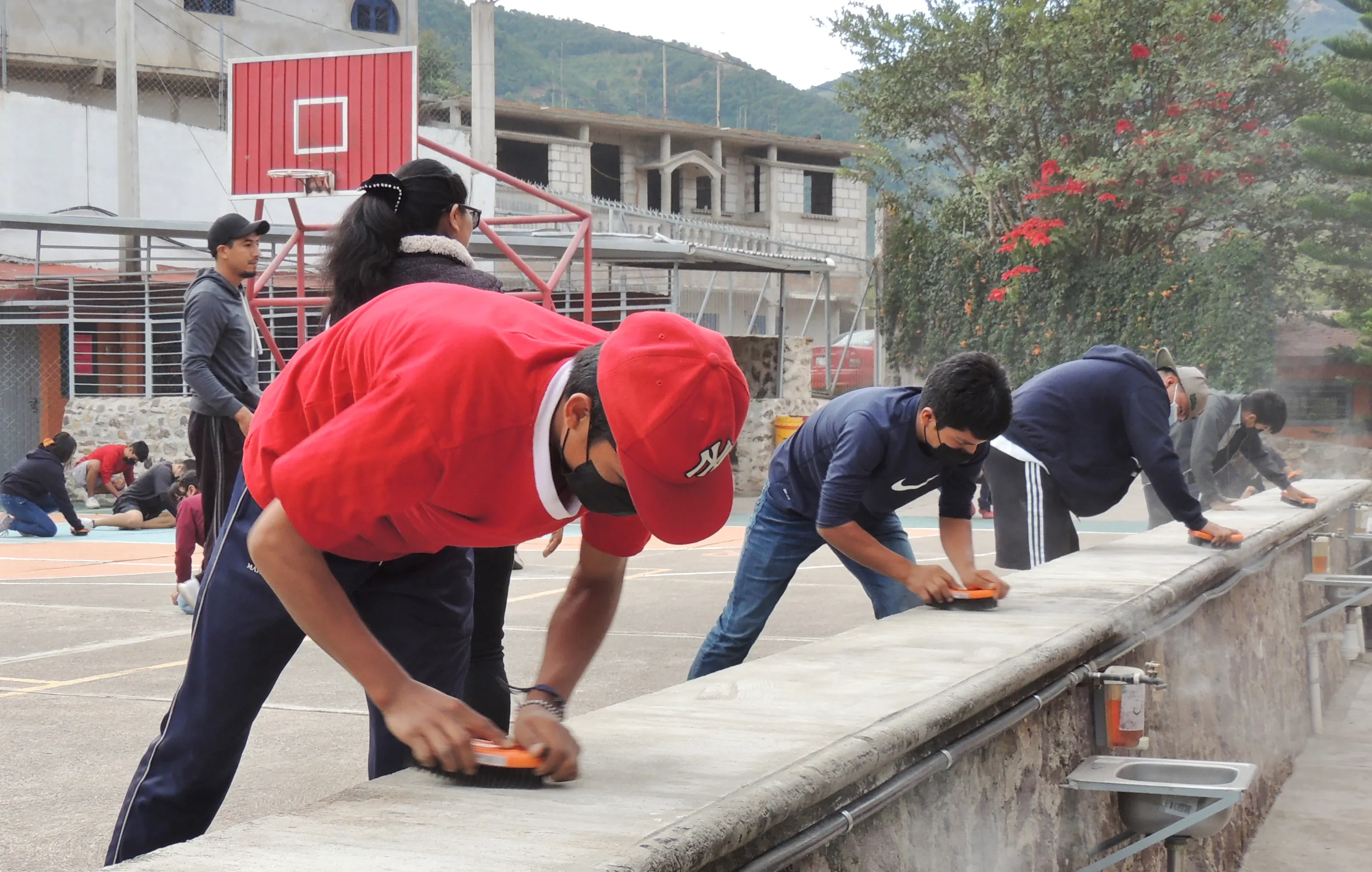 Alumnos limpiando con trapos un muro bajo junto a la cancha