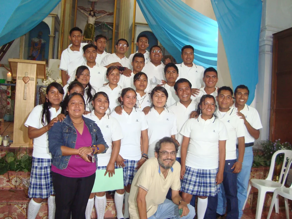 Grupo de alumnas con uniforme escolar y listones turquesa posando en un salón con cortinas