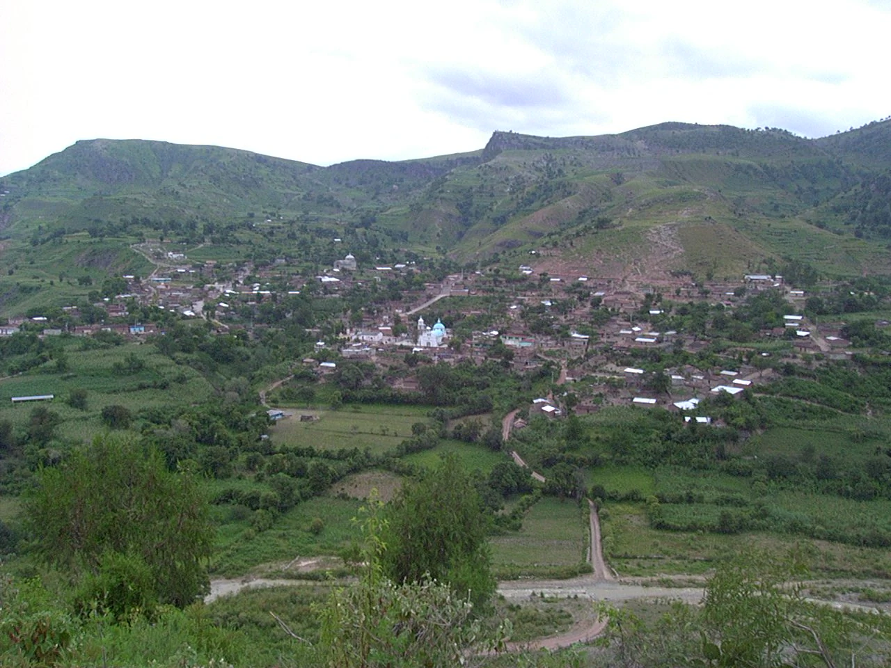 Vista del pueblo entre cerros verdes, con las casas y los campos de cultivo