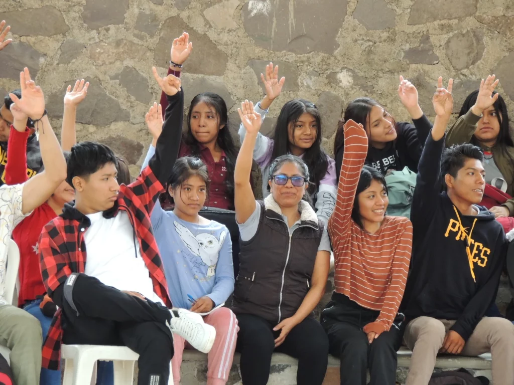 Jóvenes sentados en grupo levantando la mano durante una asamblea