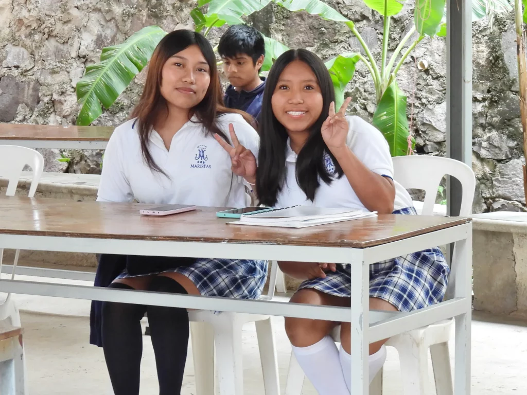 Dos alumnas con uniforme sonriendo sentadas a una mesa al aire libre