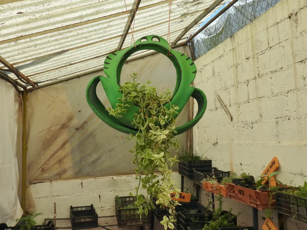 Maceta colgante hecha con una llanta pintada de verde dentro del vivero